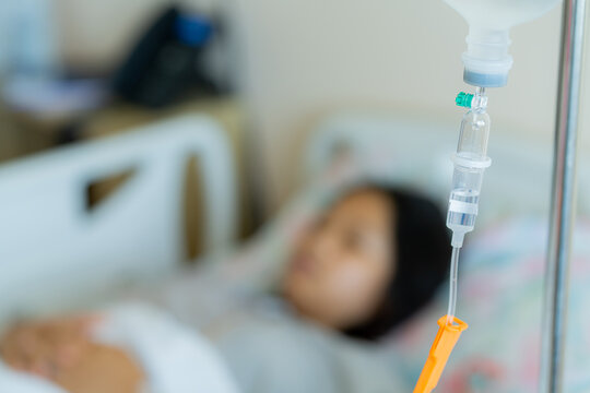 Young patient asian woman lying on the bed in hospital with IV saline drip to the back of the hand, teenager sick in hospital, Selective focus, healthcare, and health insurance concept.