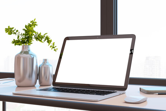 Close up of modern designer office desktop with white mock up computer screen, decorative vase with plant, other objects and window with city view in the background. 3D Rendering.