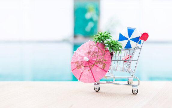 Paper umbrella with coconut tree and beach umbrella in shopping cart over blurred swimming pool background, summer sale