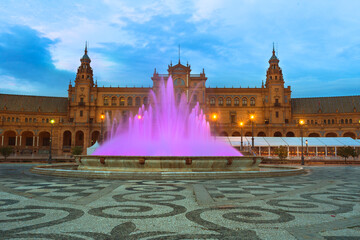 Naklejka premium At night, Plaza de Espana in Seville dazzles with an illuminated fountain, where violet waters create a mesmerizing scene, creating a captivating display that enchants visitors in this Spanish city.