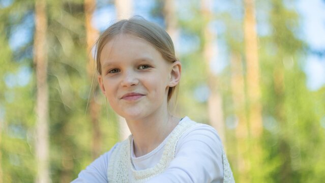 Close up head shot portrait image with smiling school aged girl. Concept happy and beauty kid on green forest background, ten year child looking at the camera
