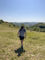 Middle-aged man wearing t-shirt and shorts hiking on meadow during summer with blue sky, holding cell mobile phone and wearing smart watch for GPS navigation, at Walberla, a hill in Franconia, Germany - 619715905