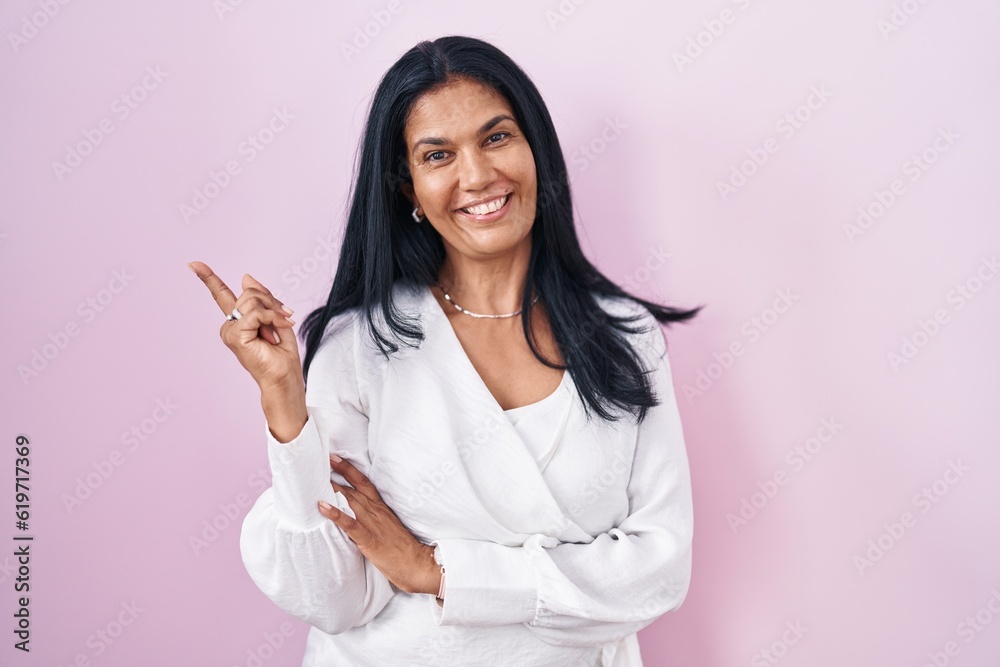 Poster mature hispanic woman standing over pink background with a big smile on face, pointing with hand fin