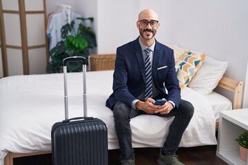 Young hispanic man business worker using smartphone sitting on bed at hotel room