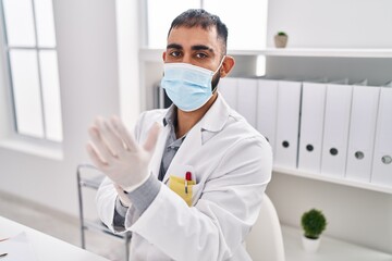 Young hispanic man doctor wearing medical mask wearing gloves at clinic