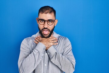 Middle east man with beard standing over blue background shouting and suffocate because painful strangle. health problem. asphyxiate and suicide concept.