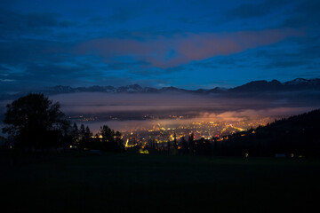 Panorama of the night city of Zakopane and the mountain range behind. Tatras and the city in the gorge. View of the night city. Lights of the night city and clouds floating above it.