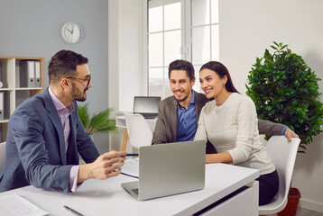 Portrait of happy caucasian couple sitting with a business broker or insurance agent showing project on a laptop screen. Clients having consultation with a man realtor or financial advisor at office. - obrazy, fototapety, plakaty