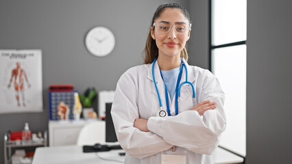 Young beautiful hispanic woman doctor smiling confident standing with arms crossed gesture at clinic