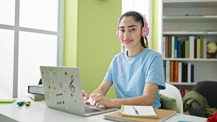 Young beautiful hispanic woman student using laptop and headphones studying at library university