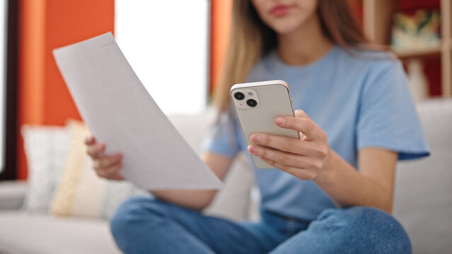 Young beautiful hispanic woman using smartphone reading paper at home