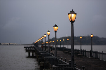 On a foggy day in San Francisco, a pier extends off into the distance, lined by antique lampposts...
