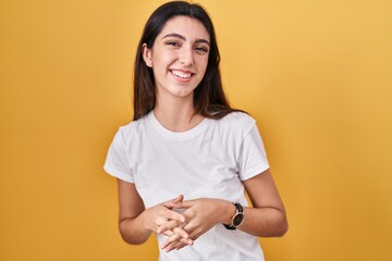 Obraz premium Young beautiful woman standing over yellow background hands together and fingers crossed smiling relaxed and cheerful. success and optimistic
