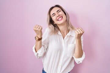 Young beautiful woman standing over pink background celebrating surprised and amazed for success...