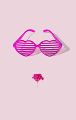 Heart shape shiny pink glasses and mouth made of pink flower on pastel pink background. Minimal creative concept of kiss, fashion, beauty, love, aesthetic. 