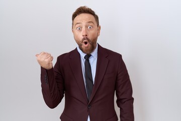 Middle age business man with beard wearing suit and tie surprised pointing with hand finger to the side, open mouth amazed expression.