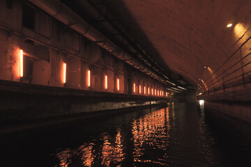 Fototapeta na wymiar Illuminated concrete tunnel with water. Abandoned underground submarine base