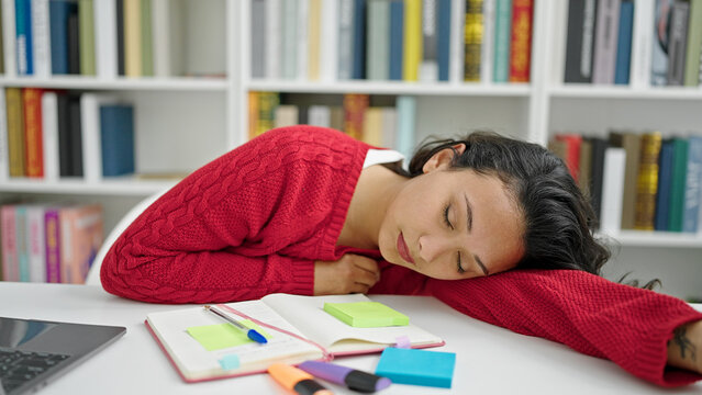 Young beautiful hispanic woman student sleeping on the desk at library university