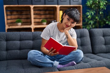 Fototapeta na wymiar Young woman reading book sitting on sofa at home