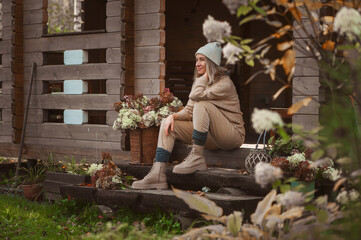 woman gardener relaxing in cozy autumn day, sitting on wooden stairs at house entryway. Enjoying warm october in the countryside, spending weekend outdoor