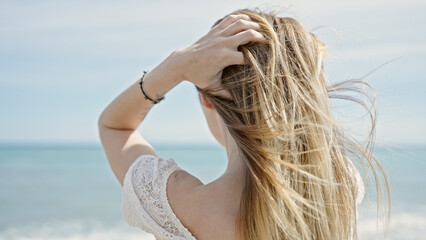 Fototapeta na wymiar Young blonde woman tourist touching hair standing backwards at beach