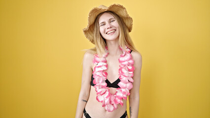 Young blonde woman tourist wearing bikini and hawaiian lei smiling over isolated yellow background