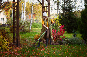 seasonal autumn garden work. Woman gardener raking fall leaves - obrazy, fototapety, plakaty