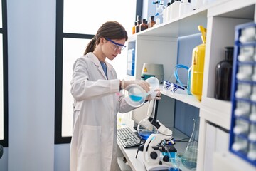 Young blonde woman scientist pouring liquid on test tube at laboratory