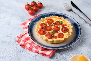 Unsweetened shortbread tartlets with feta cheese, cherry tomatoes and herbs on a blue plate on a light concrete background.
