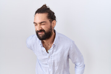 Hispanic man with beard wearing casual shirt suffering of backache, touching back with hand, muscular pain