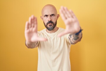 Fototapeta premium Hispanic man with tattoos standing over yellow background doing frame using hands palms and fingers, camera perspective