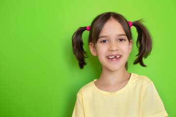 Close-up portrait of happy laughing cute toddler girl with missing baby tooth smile over green