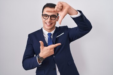 Young hispanic man wearing suit and tie smiling making frame with hands and fingers with happy face. creativity and photography concept.