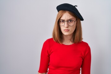 Young redhead woman standing wearing glasses and beret skeptic and nervous, frowning upset because of problem. negative person.