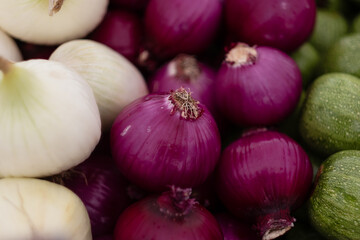 White onions, red onions, and zucchini stacked up for sale at a farmers market.