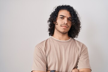 Hispanic man with curly hair standing over white background skeptic and nervous, disapproving expression on face with crossed arms. negative person.