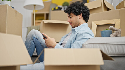 Young latin man using smartphone sitting on floor at new home