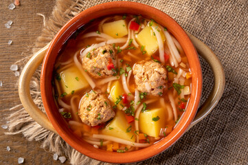 Meatballs soup with noodles and vegetables, romanian traditional food. wooden background. Ciorba de...