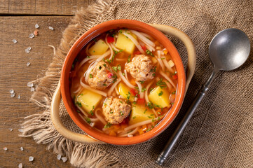 Meatballs soup with noodles and vegetables, romanian traditional food. wooden background. Ciorba de...