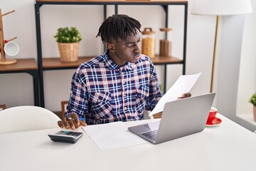 African american man using laptop reading document accounting at home