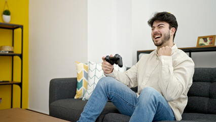Young hispanic man playing video game sitting on sofa at home