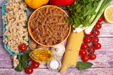 Italian pasta with vegetables, olive oil, spices on a wooden background,top view.