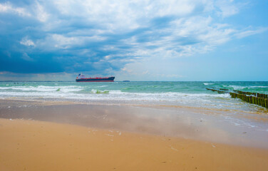 Sand beach along a sea under a dark blue cloudy sky in bright sunlight in summer, Zeeland, the Netherlands, June, 2023