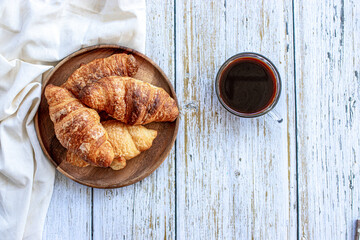 A cup of coffee and croissant on white table.