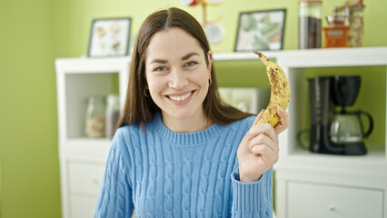 Young caucasian woman holding banana sitting on table at dinning room