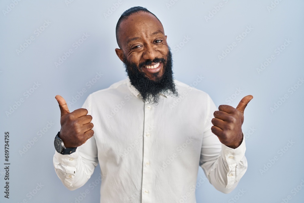 Poster African american man standing over blue background success sign doing positive gesture with hand, thumbs up smiling and happy. cheerful expression and winner gesture.