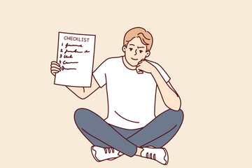 Man demonstrates checklist recommending time management and organizing own work. Smart smiling guy is sitting and holding checklist with tasks for day or step-by-step plan to achieve goal in hand