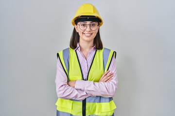 Hispanic girl wearing builder uniform and hardhat happy face smiling with crossed arms looking at the camera. positive person.