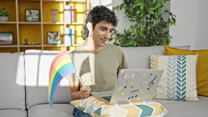 Naklejka premium Young hispanic man holding rainbow flag having video call at home