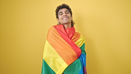 Young hispanic man smiling confident wearing rainbow flag over isolated yellow background